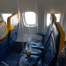 This undated photo provided by the National Transportation Safety Board on Thursday, Aug. 13, 2026, shows the shattered window on a Ryanair plane that was broken by a stray engine part shortly after takeoff, causing a man's head to be sucked into the hole. (National Transportation Safety Board via AP)